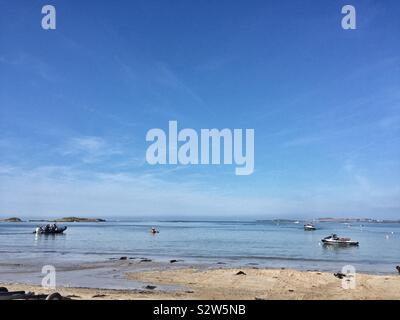 Boote auf dem Wasser bei Flut auf einem ruhigen Tag in Rhosneigr, Traeth Crigyll, Anglesey, Nordwales Stockfoto