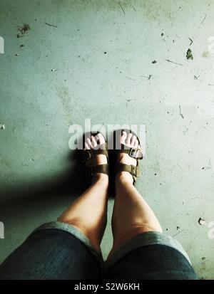 Mit Blick auf die Beine der Frau und die Füße tragen Denim Shorts und Sandalen aus Leder Stockfoto