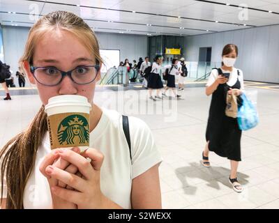 Junge kaukasier Jugendmädchen trinken aus einem Takeaway Starbucks Coffee Cup in einer U-Bahn Station in Japan. Stockfoto