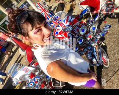 Brighton, UK. Ein Mädchen, das in den sechziger Jahren Periode Kleidung Lächeln neben einer angepassten Scooter als Mods aus ganz Großbritannien für die jährliche August Bank Holiday Mod Weekender Rallye in der Sonne sammeln. Stockfoto