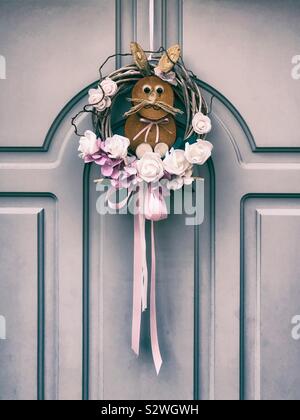 Dekorativer Kranz mit Holz- Bunny und Blumen hängend an einer Vordertür Stockfoto