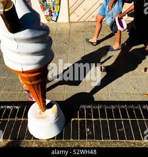 Ein Strand Strandpromenade Szene, Füße und Beine Schatten von Menschen zu Fuß vorbei an einem Eis Kiosk große Kegel Werbung Modell Stockfoto