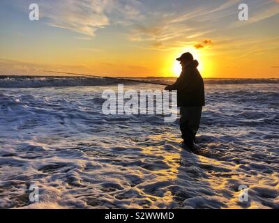 Silhouetted angler angeln in der Brandung am Llangennith, Gower, Swansea, South West Wales, August. Stockfoto