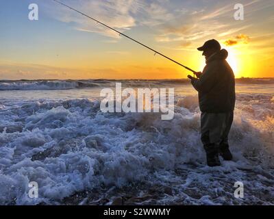 Angler Angeln in der Brandung bei Sonnenuntergang auf llangennith Strand, Gower, Swansea, South West Wales, August. Stockfoto