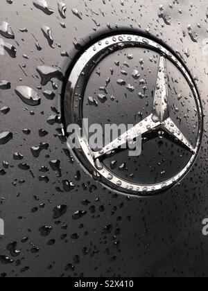 Eine Nahaufnahme eines Mercedes Benz Car Logo auf der Rückseite eines metallischen Matt schwarze Auto im Regen Stockfoto