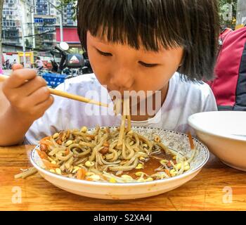 Eine wunderschöne junge asiatische chinesische Mädchen essen und genießen ein Köstliche Schüssel mit Nudeln Stockfoto