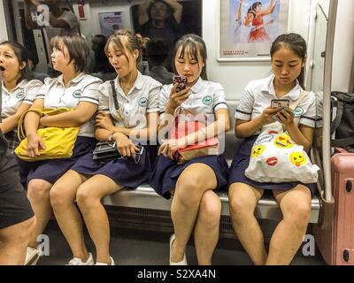 Asian Chinese schoolgirls sitting on the Beijing metro on their way home after school checking their phones and social media feeds Stock Photo