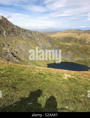 Schatten von zwei Menschen, die auf ihrer Wanderung auf einen Berg mit Blick auf einen kleinen Tarn Stockfoto