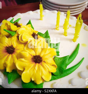 Blick von oben auf eine Geburtstagstorte mit gelben buttercream Blumen und ihre Blätter mit sieben Kerzen ausgeblasen wurden abgedeckt. Stockfoto