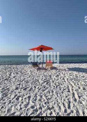 Zwei bunte Liegestühle und Sonnenschirm von hinten sitzen auf weißen Sandstrand mit Blick auf türkisblaues Wasser und blauer Himmel Stockfoto