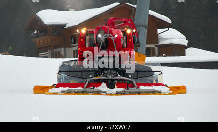 Eine rote Pistenfahrzeug startet die Skipisten für seine Mission vorzubereiten. Die Maschine aus Tirol in Österreich können von der Vorderseite gesehen werden und hat seine Lichter an. Stockfoto