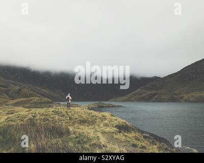 Frau in Wandern Kleidung über See vor der nebligen Bergen suchen Stockfoto