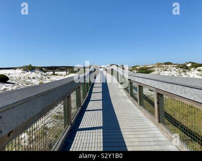 Langen Holzsteg, der zum Strand führt mit Schatten und weißen Sanddünen mit blauer Himmel Stockfoto