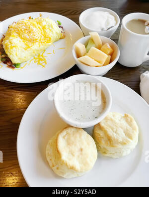 Hausgemachte buttermilk Biscuits mit Gravy. Es gibt auch ein Ei, Omelett und eine Schale mit frischem Obst. Kaffee ist das Getränk der Wahl. Stockfoto