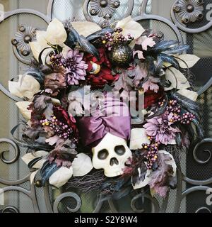 Halloween Kranz mit Schädel und lila Blüten und Blätter hängen an einem dekorativen schmiedeeisernen Tor Stockfoto