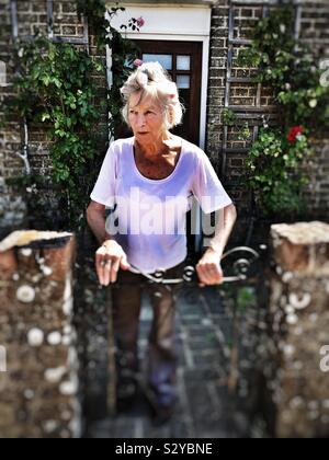 Alter Rentner in Ihrem Garten Tor stehend, Bawdsey, Suffolk, England. Stockfoto