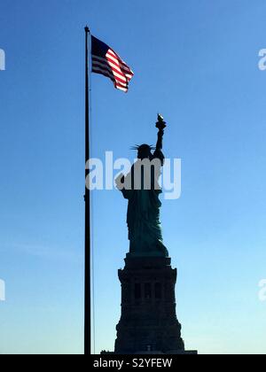 Die Freiheitsstatue und die amerikanische Flagge als von Liberty Island, New York City, USA Stockfoto