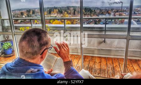 Mann lesen Buch über Hochhaus geschlossene Terrasse mit Panoramablick, Schweden Stockfoto