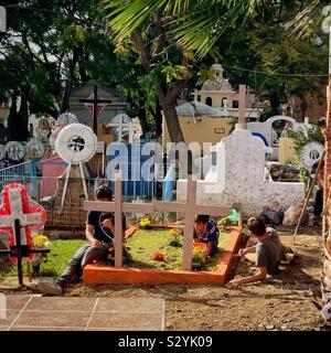 Drei junge Männer bereiten eine Familie Grabstätte für Día de los Muertos. Stockfoto