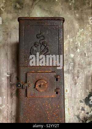 Mit einem alten, rostigen Holzofen gegen eine Betonwand in einem verlassenen Bauernhaus. Stockfoto