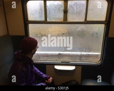 Ein Mann sitzt in einem altmodischen Waggon Blick aus dem Fenster an einem kalten regnerischen Wintern Tag Stockfoto