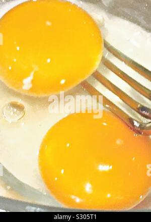 Zwei Eier in ein Glas Schale, Eigelb und Eiweiß, mit einer Gabel aus Metall Stockfoto