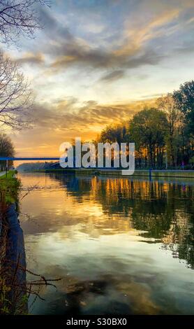 Dramatische und farbenfrohen Sonnenaufgang oder Sonnenuntergang Himmel über ein Kanal von Fluss, der durch einen Wald Landschaft, auf der Oberfläche des Wassers wider Stockfoto