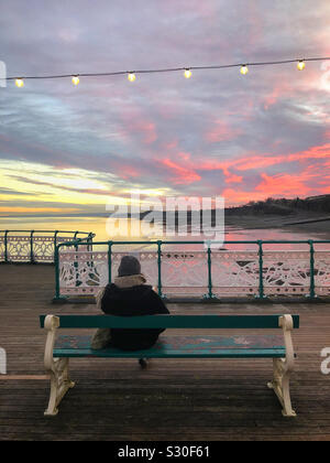 Eine Dame genießen den Sonnenuntergang von Penarth Pier, während ein Buch lesen, South Wales, Dezember. Stockfoto