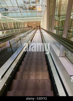 Eine lange Rolltreppe nach unten im Terminal 2, Flughafen München, Deutschland. Diese Links zu den fahrerlosen Shuttle für die Weitergabe an die T2-Satelliten. T2 war angeblich "Nummer eins der Welt terminal" im Jahr 2017. Stockfoto