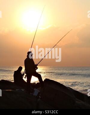 Ein paar Fischer von der aufgehenden Sonne steht auf Felsen am Meer. Stockfoto
