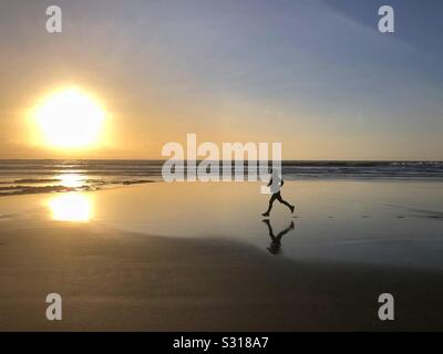 Junge Frau in einem sandigen Strand bei Sonnenuntergang, South Wales, Januar.