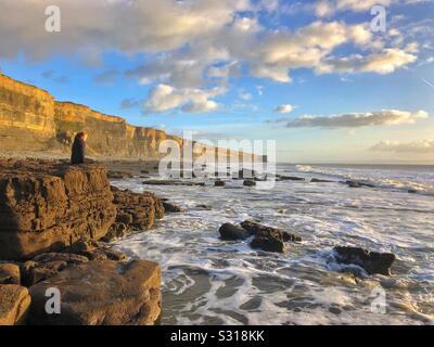 Junge Frau genießen den Blick über das Meer auf Traeth Mawr, Glamorgan Heritage Coast, South Wales, Januar. Stockfoto