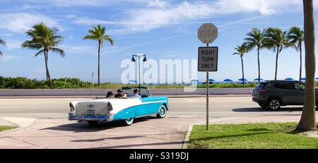 Eine restaurierte 1956 Chevy Bel Air convertible zieht von einem Hotel in Florida auf die Landstraße entlang des Strandes. Stockfoto