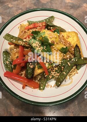 Veganer Hauptgericht-knuspriger Tofu mit roten Paprika für Schneepäen und Mangosalsa mit gehackten Erdnüssen über Nudeln. Stockfoto