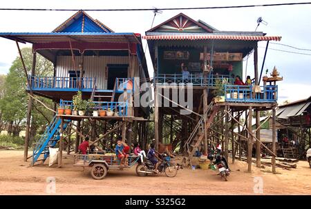 Traditionelle Doppelhäuser und Kinder, die einen Motorradwagen in Kompong Khleang Dorf, Tonle Sap See, Siem Reap, Kambodscha fahren Stockfoto