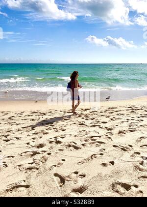 Frau und eine Möwe, die am Strand entlang der Meereswellen spazieren geht, USA. Stockfoto