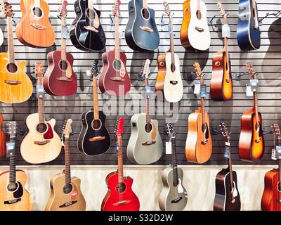 Akustische Gitarren in verschiedenen Farben hängen an der Wand zum Verkauf im Musikladen Stockfoto