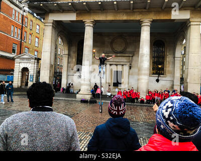 Touristen, die einen Straßendarsteller auf einem Einrad vor der St Paul's Church, Covent Garden, London, England beobachten Stockfoto