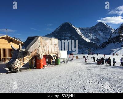 Skigebiet Männlichen mit Holzkuh, in Rückenmtnen. Eiger (l) und Mönch, Grindelwald, Schweiz. Stockfoto