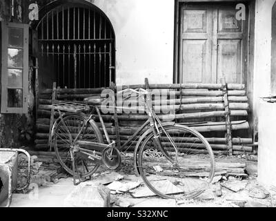 Ein altes Gebäude, das für das Haufen von Sachen benutzt wird, ein altes Fahrrad, Bambusstangen alter Metallstuhl, kaputte Tonfliesen mit gegrilltem Fenster und Holztür, ein klassischer Vintage-Look Stockfoto