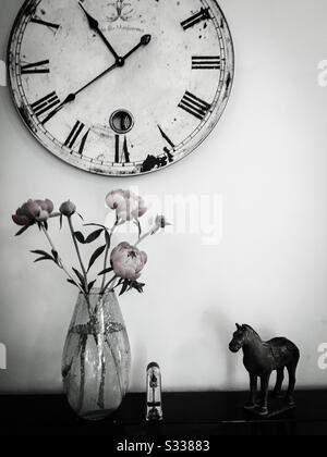 Ein Schwarz-Weiß-Stilllebenfoto aus einer Uhr, orientalischem Pferdeornament, Metronom und einer Vase aus pfirnigen Blumen, die alle auf einem Klavier platziert sind. Stockfoto