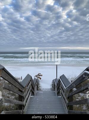 Holzsteg zum Strand mit pfiffigen weißen Wolken am Himmel Stockfoto