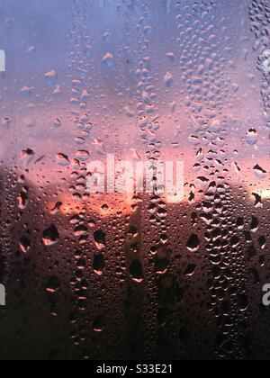 Kondensation (Wassertröpfchen) an einem Fenster in der Nähe, mit einer rosa und violetten Dämmerung Farben im Himmel durch ihn betrachtet. Stockfoto