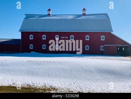 Dubuque, IOWA, 23.02.20 Landschaftlich schönes Foto von schöner roter Scheune mit weiß gerahmten Fenstern mit schneebedecktem Dach unter hellblauem Himmel an einem sonnigen Tag. Stockfoto