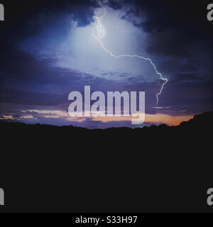 Ein Lichtschlag bei einem Gewitter am Abend. Dämmerungsstunden mit dunklen Bäumen am Horizont und Kopierraum Stockfoto