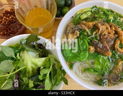 Eine Mahlzeit mit vietnamesischen Pho- oder Reisnudeln mit Gemüse und einem Glas Tee Stockfoto