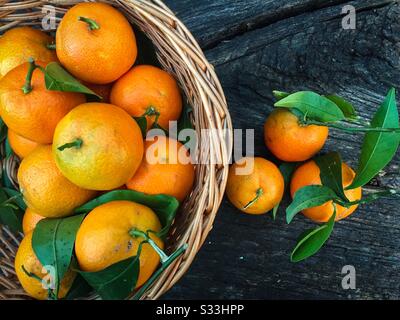 Mandarinen mit Blättern in einem Korb auf rustikalem Holztisch Stockfoto