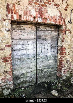 Sehr alte verblichene graue Holz-Doppelscheune-Türen, umgeben von roten Backsteinen und beigefarbenem Betonstuck. Stockfoto