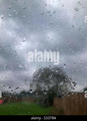 Blick durch ein Glasfenster. Bedeckt mit Regentropfen an einem regnerischen Tag in einem Garten darüber hinaus. Stockfoto