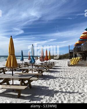 Picknicktische im Freien am weißen Strand mit bunten Stühlen und Sonnenschirmen Stockfoto